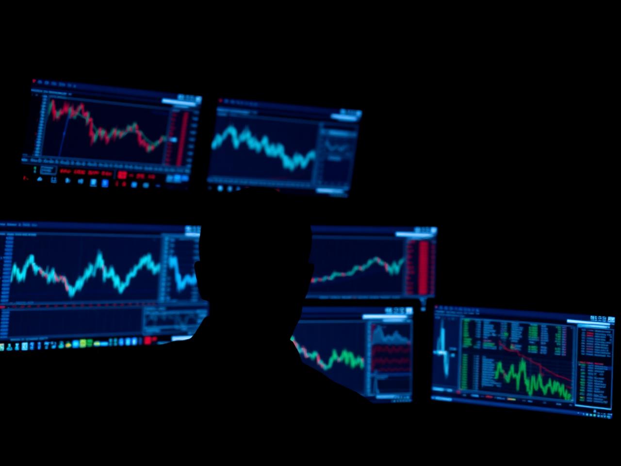 Multi-monitor trading desk with tick charts glowing blue in a dark room